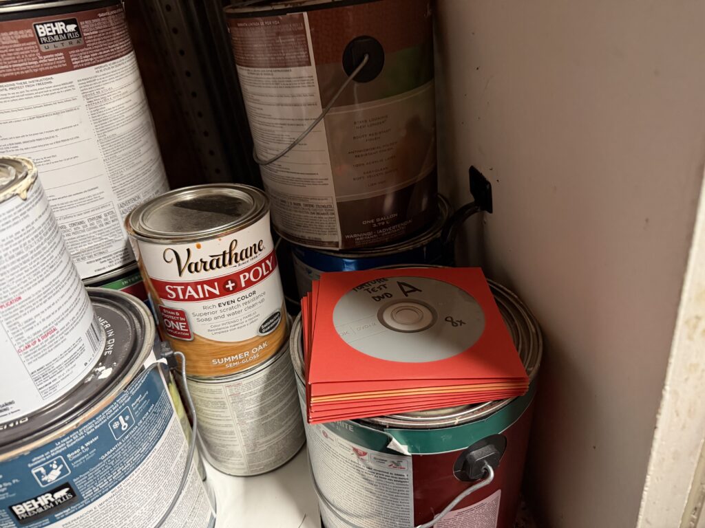 A pile of discs in red and orange sleeves on top of a can of paint in a dirty looking shed
